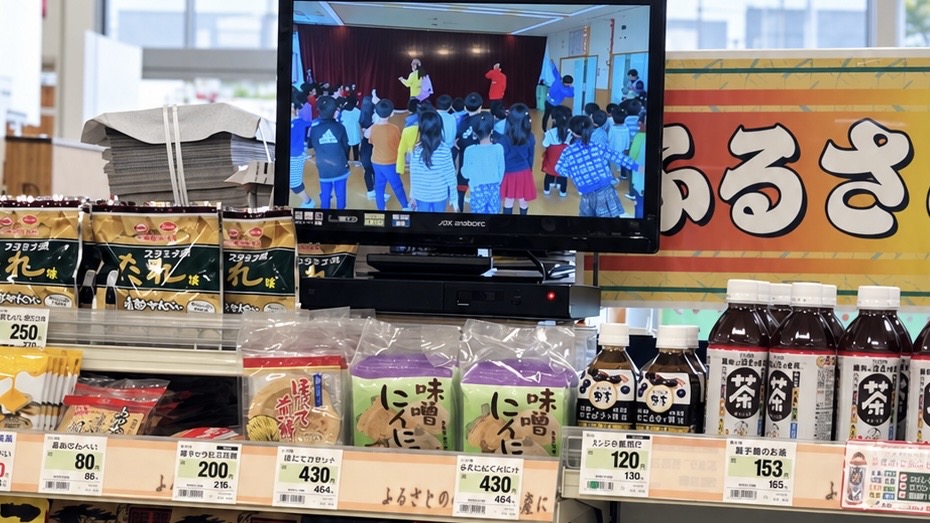 よこまちストアの食品売り場のモニターで流れる「おんでやんせ八戸」の園児とのダンス場面