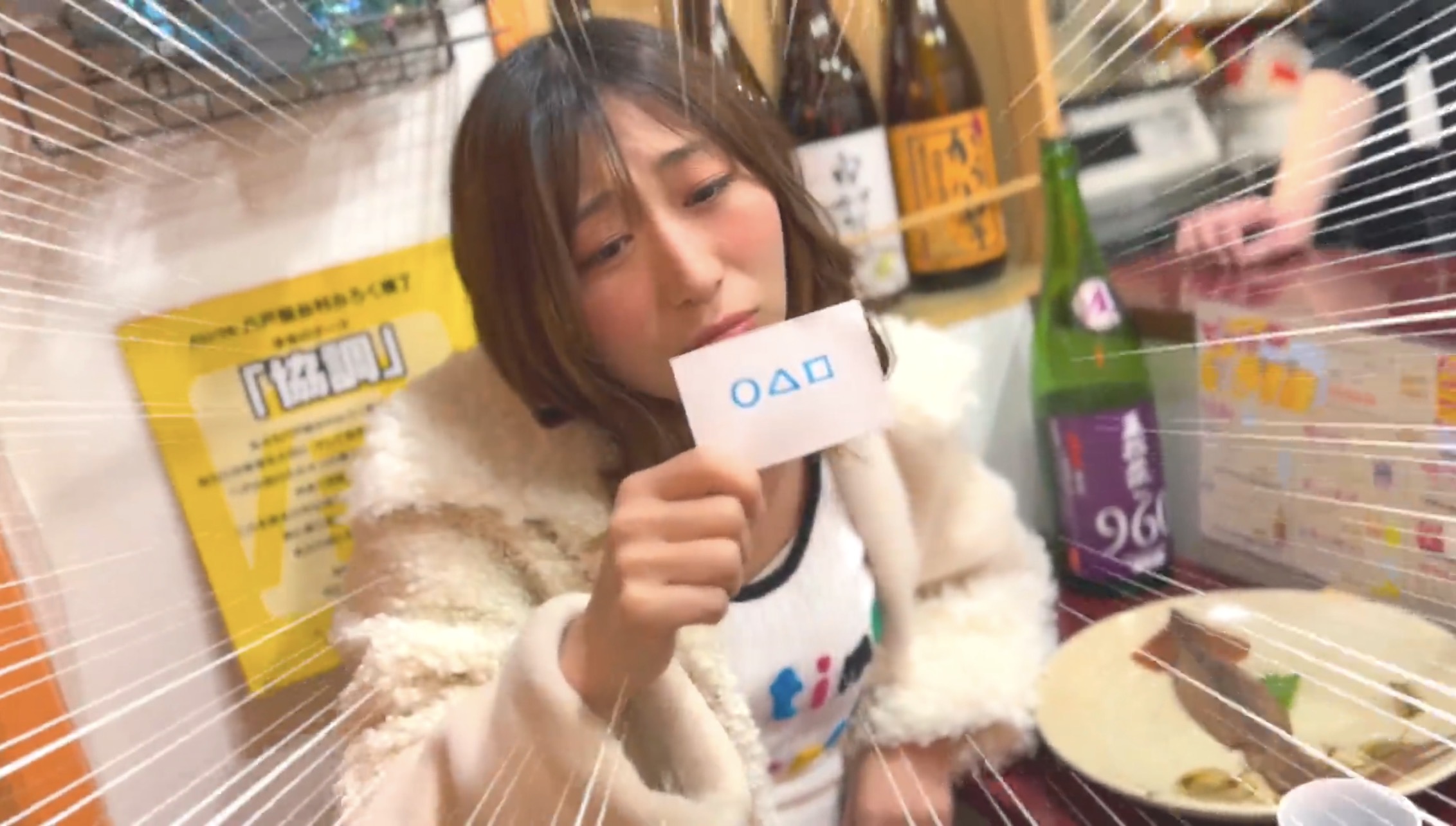 みろく横丁の店内で、番号札を手に酔っ払い役を演じるJunko☆
